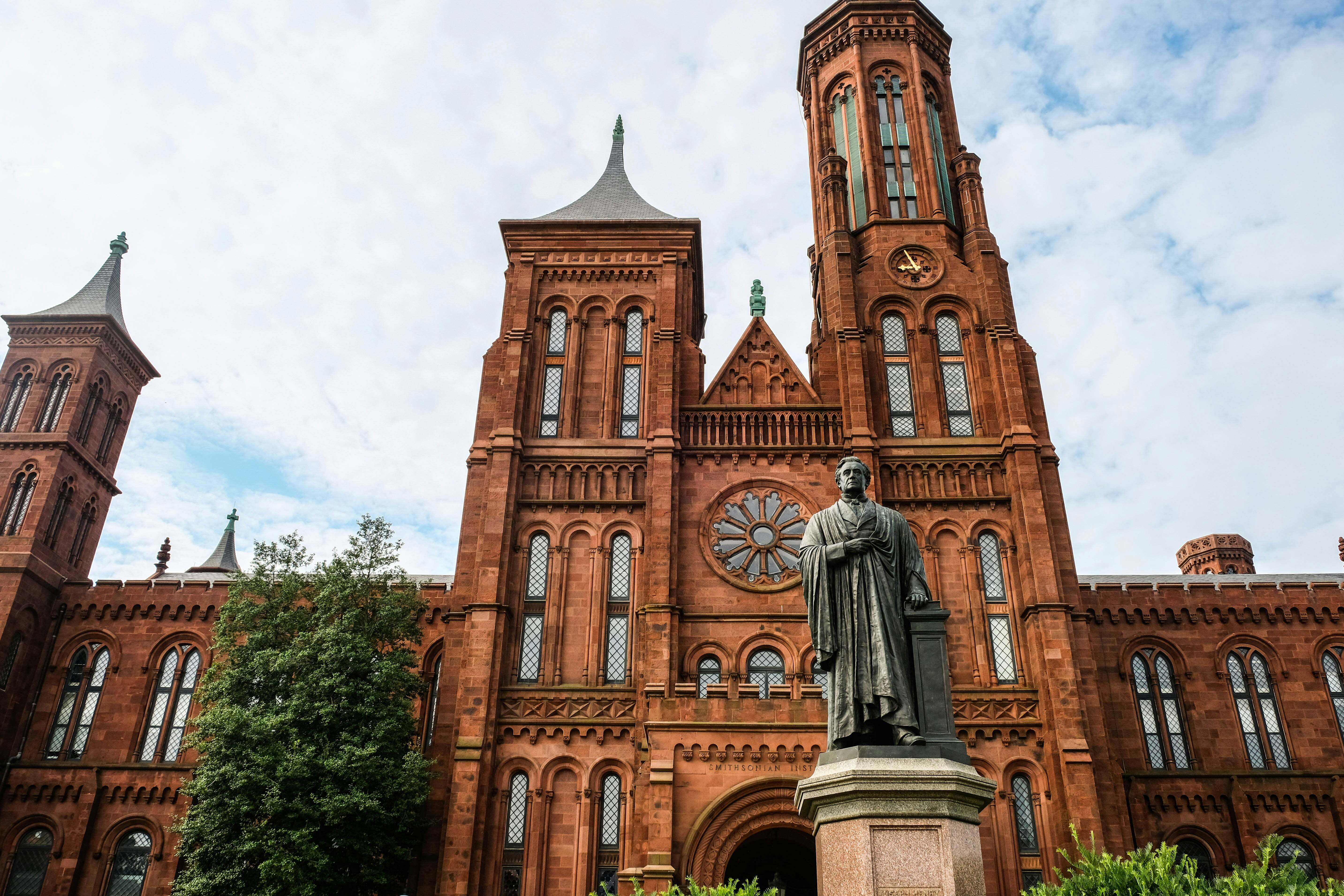 The Smithsonian Institution Building, known as the Smithsonian Castle, made of red sandstone with two tall towers, seen from the front with a statue of Joseph Henry