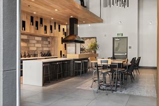 Chef’s kitchen and private dining room with a long quartz island, wood-paneled walls, textured tile backsplash, black range hood, bar seating, and a large dining table under modern pendant lighting.