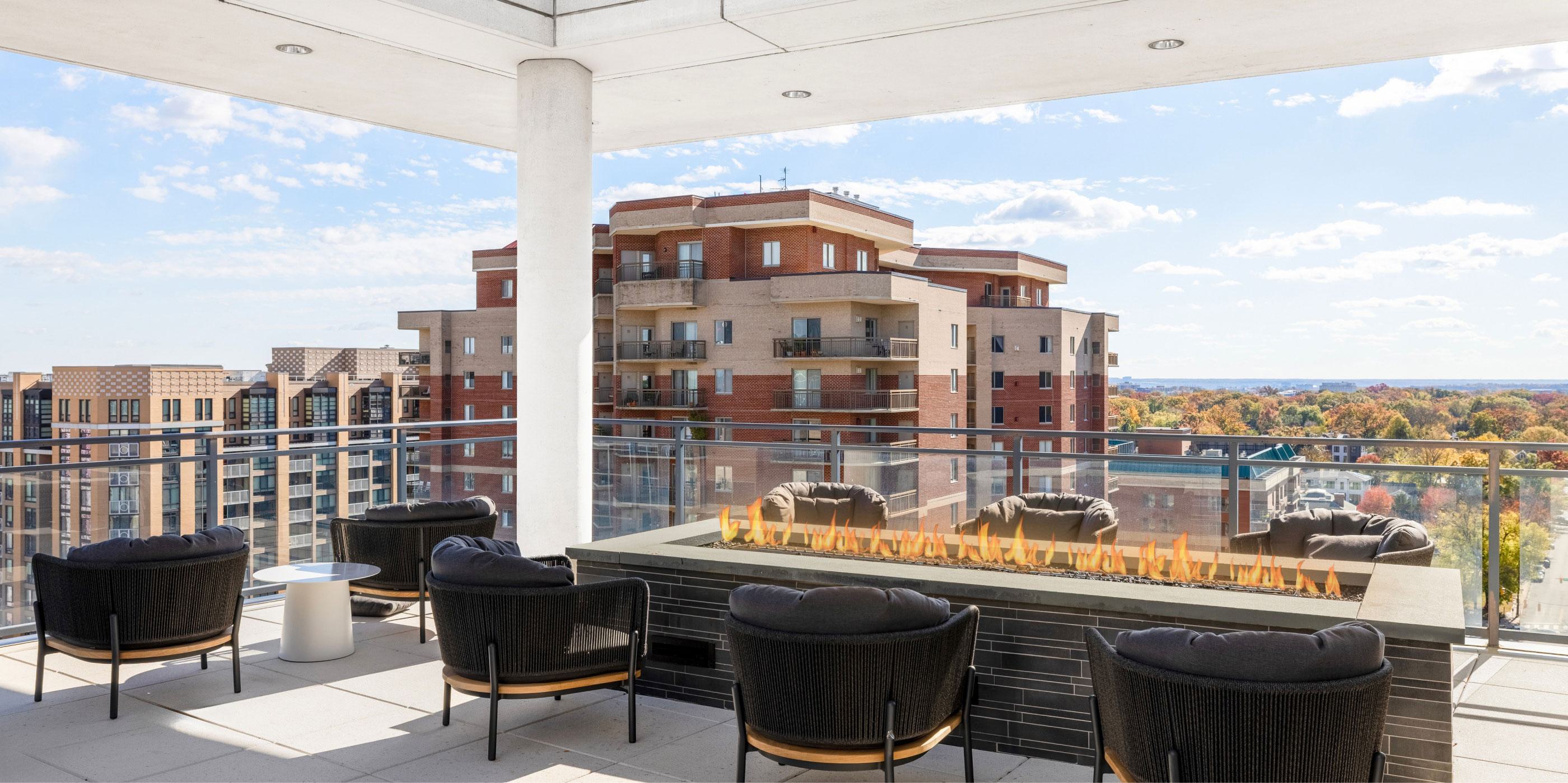 Rooftop lounge at Latitude Apartments in Virginia Square with a modern linear fire pit, cushioned seating, glass railings, and expansive neighborhood views.