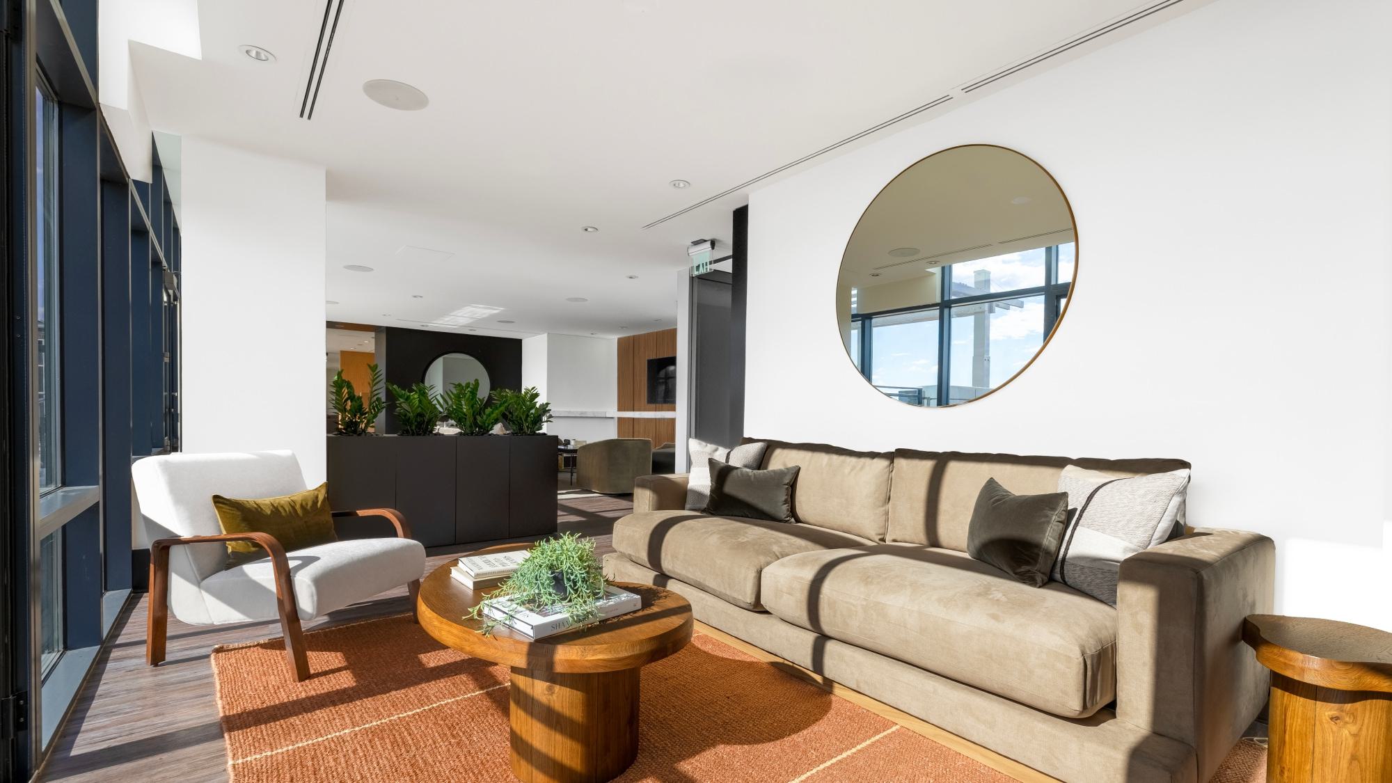 Sunlit resident lounge at Latitude apartments featuring modern seating, warm wood accents, floor-to-ceiling windows, and layered communal gathering spaces.