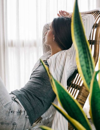A woman lounging on a rattan chair in a room with filtered light