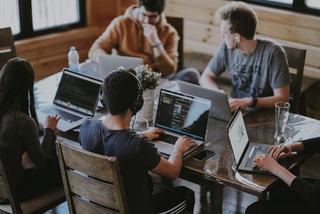 workers on laptops in a casual industrial setting with wooden table