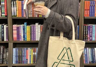 woman browsing at a bookstore holding a coffee and an arlo book bag