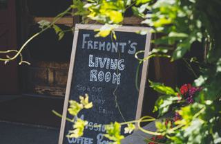 Chalkboard sign reading “Fremont’s Living Room” outside a neighborhood café, framed by greenery and flowers in Fremont, California.