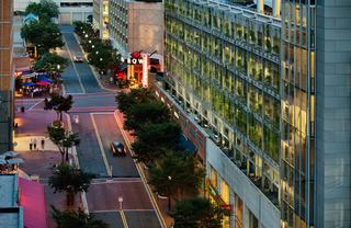 Elevated evening view of Reston Town Center showing a tree-lined street with restaurants and outdoor dining, modern buildings with lit offices, and a vertical garden façade along a multi-level parking structure.