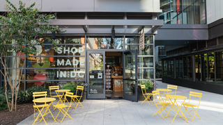 Ground-floor retail storefront in the Union Market District with a glass façade reading “Shop Made in DC,” open doors, and bright yellow café tables and chairs arranged on the sidewalk seating area.
