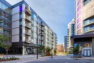 Streetscape view of The Gantry apartments in Washington, DC, showing modern mid-rise buildings with balconies, ground-floor retail, wide sidewalks, and landscaped public space in the NoMa neighborhood.