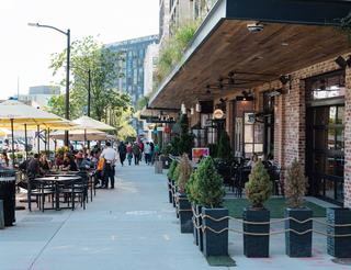 Active sidewalk dining along 4th Street NE in Washington, DC, with restaurants and cafés in the Union Market District, outdoor tables, umbrellas, and pedestrians moving through a lively mixed-use corridor