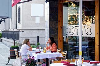 Outdoor sidewalk dining at a wine bar in downtown Stamford, Connecticut, with two people seated at a white tablecloth table beside a glass-fronted restaurant.
