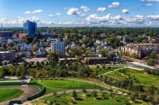 Aerial view of Mill River Park in downtown Stamford, Connecticut, showing expansive green lawns, winding walking paths, and surrounding residential neighborhoods with the city skyline in the background.