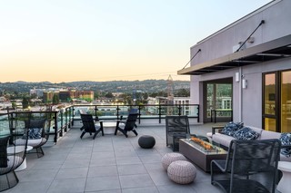 Rooftop terrace at One Adrian Burlingame with modern lounge seating and a fire table, overlooking the city skyline and surrounding Peninsula hills at sunset.