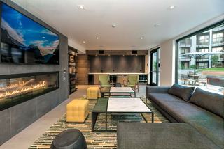Fireside resident lounge with a wall-mounted linear fireplace, large TV, modern seating, and floor-to-ceiling windows opening to an outdoor courtyard at Fourth Street East Apartments.