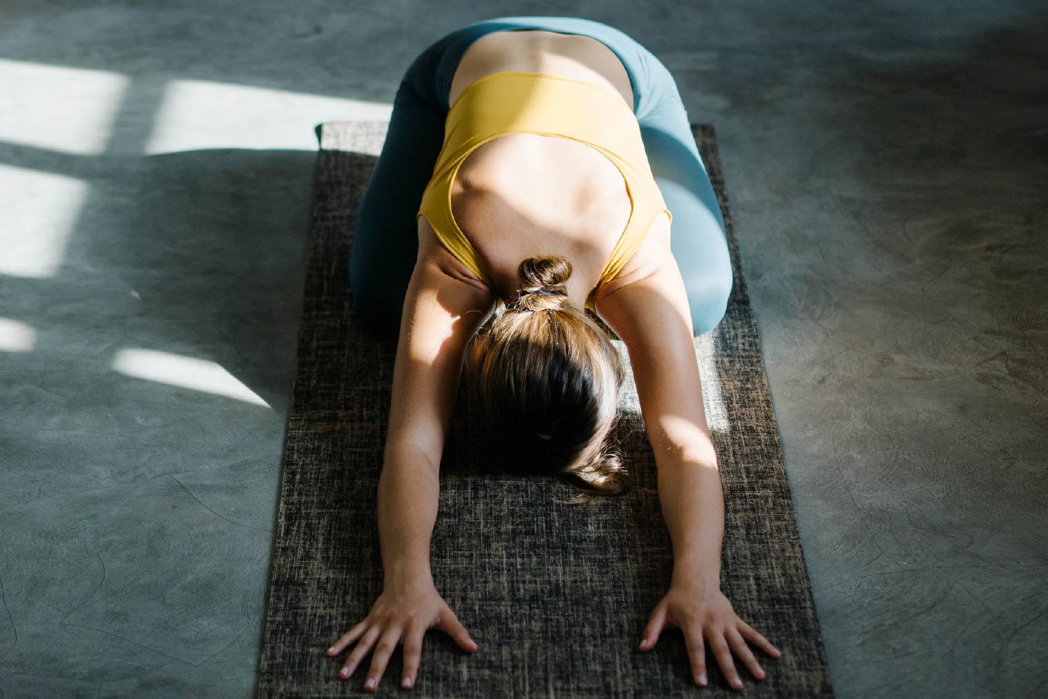 A woman practices yoga on a mat in a sun-drenched fitness studio at The Bowden, showcasing the wellness amenities available at these Redmond apartments.