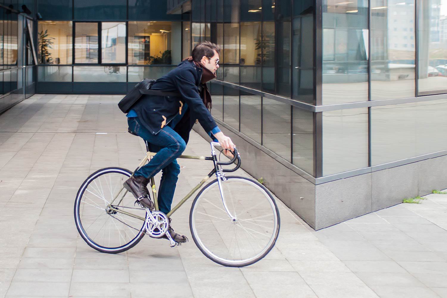 A resident commutes by bicycle past a modern glass building near The Bowden apartments, highlighting the bikeable lifestyle of the Overlake technology corridor in Redmond.
