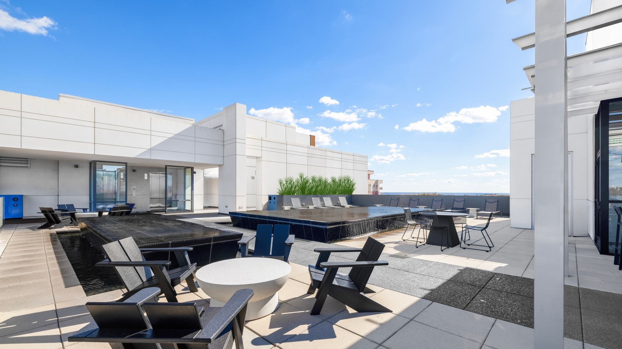A rooftop terrace with tiered black stone water features, Adirondack chairs, and modern outdoor dining sets.