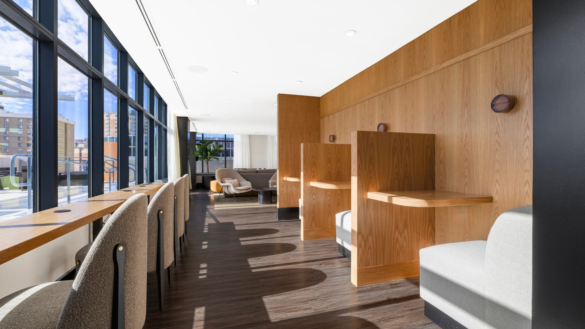 The rooftop coworking lounge showing private wooden work booths with bench seating and a long wooden window bar counter facing panoramic city views.