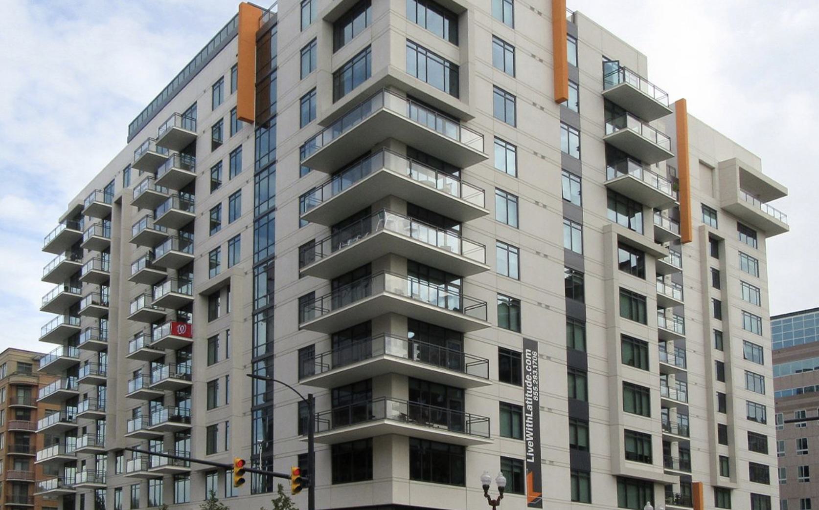 Exterior view of Latitude apartments in Virginia Square, showing the modern high-rise with balconies at a corner intersection in Arlington at dusk.