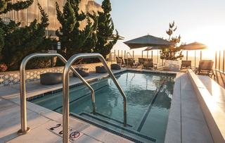 Rooftop spa at ARQ on the 31st floor with glass railings, long rectangular spa, lounge seating, and sunset views over Los Angeles