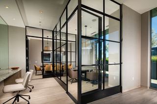 Glass-walled meeting rooms and coworking space at VOX with shared tables, task chairs, and black-framed partitions next to the Great Room