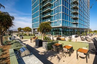 ARQ’s landscaped courtyard with outdoor dining tables, built-in grill stations, tiled planters, and a pétanque court