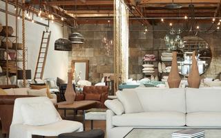 Cisco Home Culver City showroom with layered sofas, leather chairs, sculptural wood vases, and hanging pendant lights under exposed wood ceilings