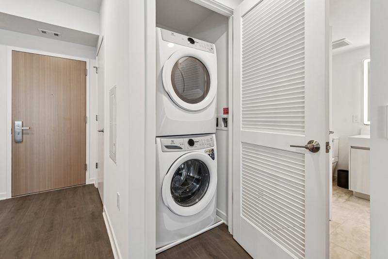Stacked white washer and dryer inside a dedicated laundry closet at Aerie, with louvered door and wood-style flooring nearby.