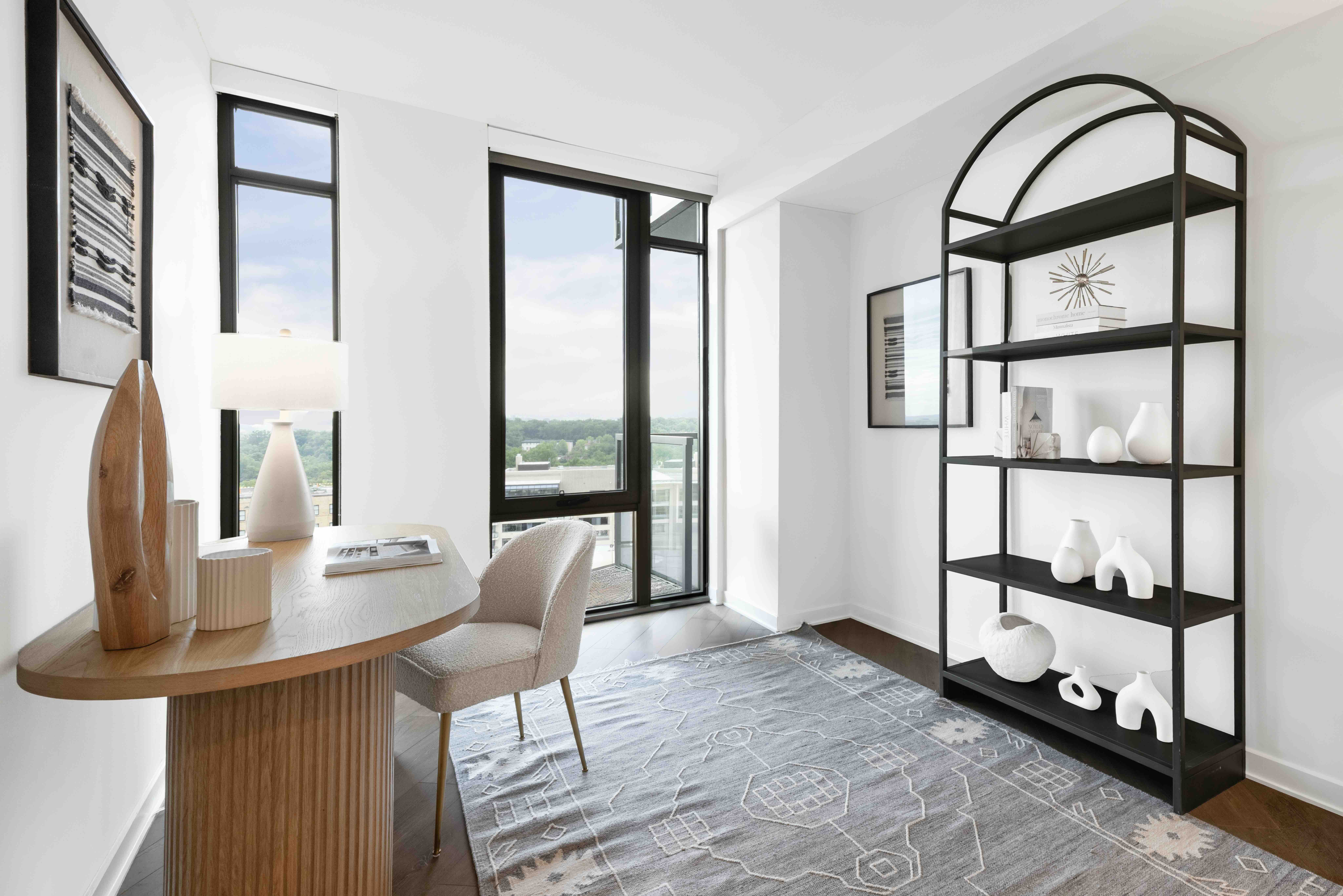 Home office at Aerie with a wood desk and drawer base, large window and balcony access, modern art, and a lounge sofa in a bright, flexible den space.