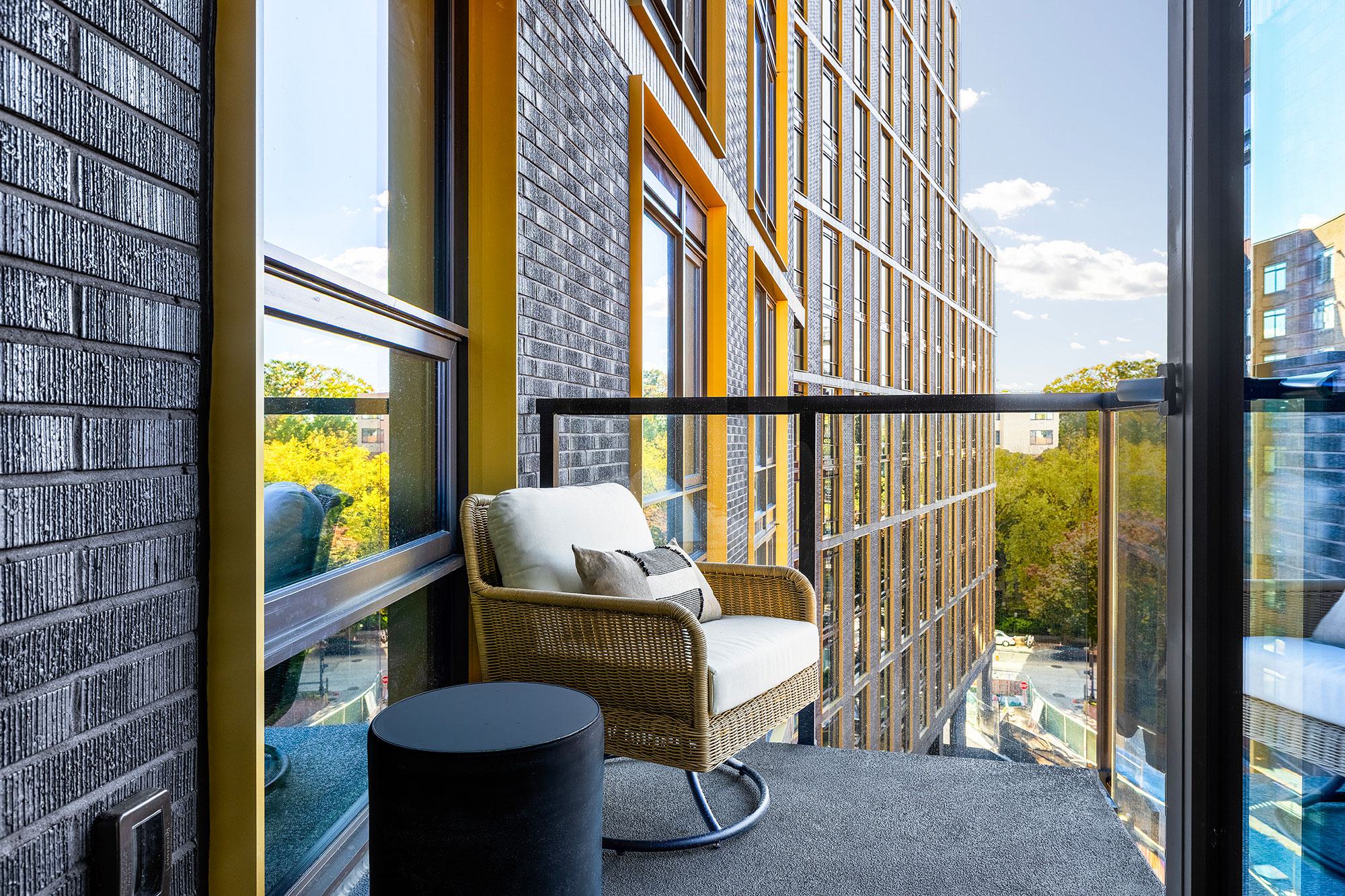 Private balcony at Zephyr with woven lounge chair, glass railing, brick façade detailing, and views over Woodley Park.