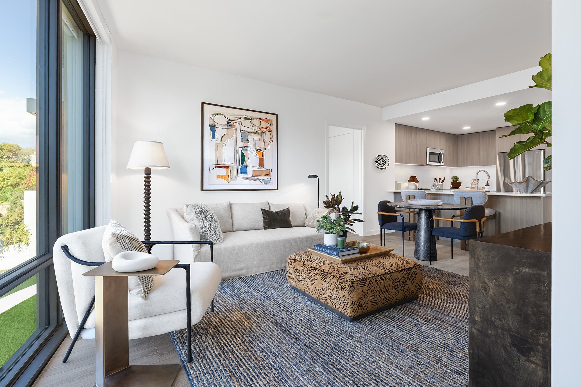 Living room at Zephyr with floor-to-ceiling windows, open kitchen with peninsula seating, and natural light throughout.