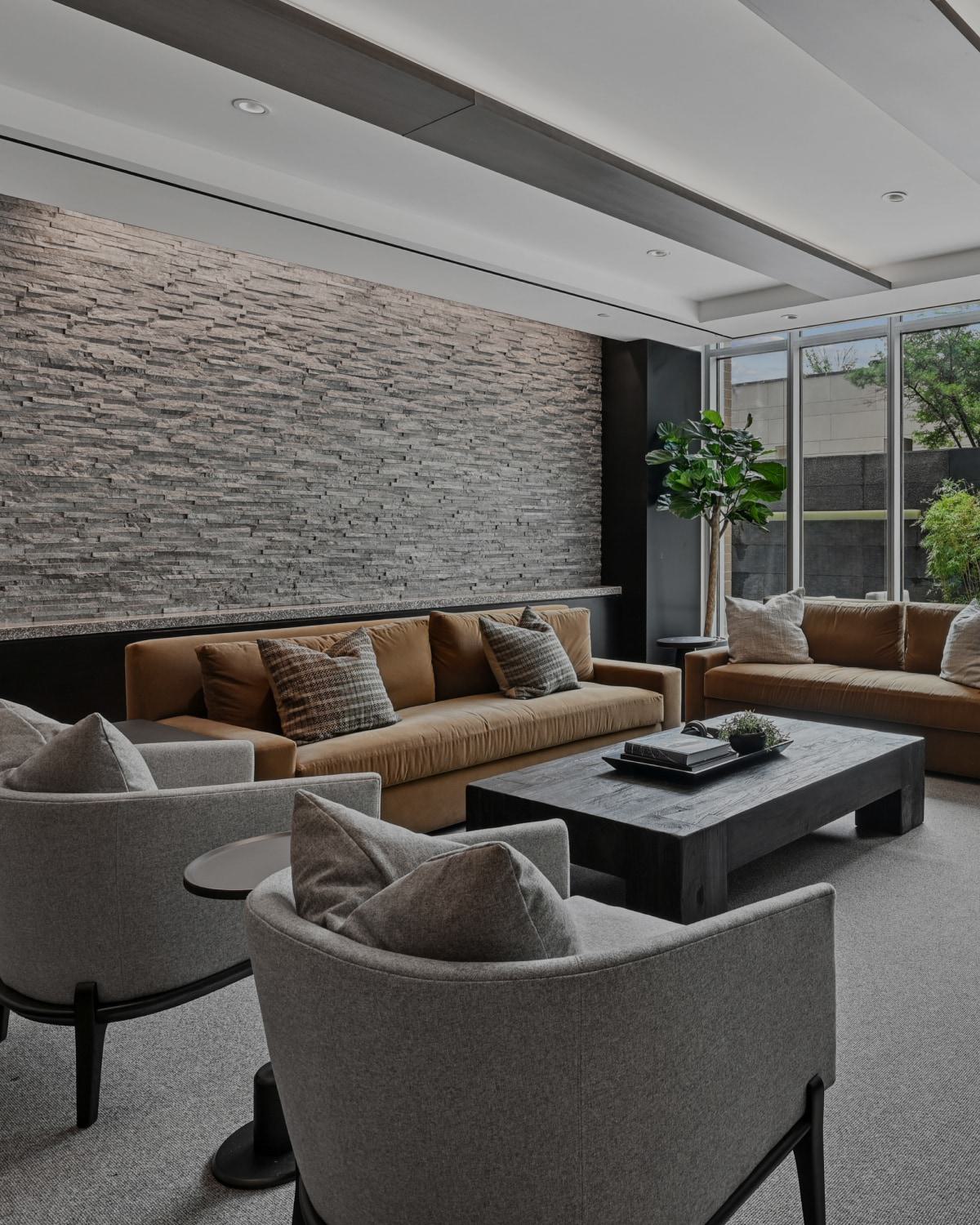 Modern resident lounge at Avant Reston featuring brown sofas, grey armchairs, a stone accent wall, and patio views.