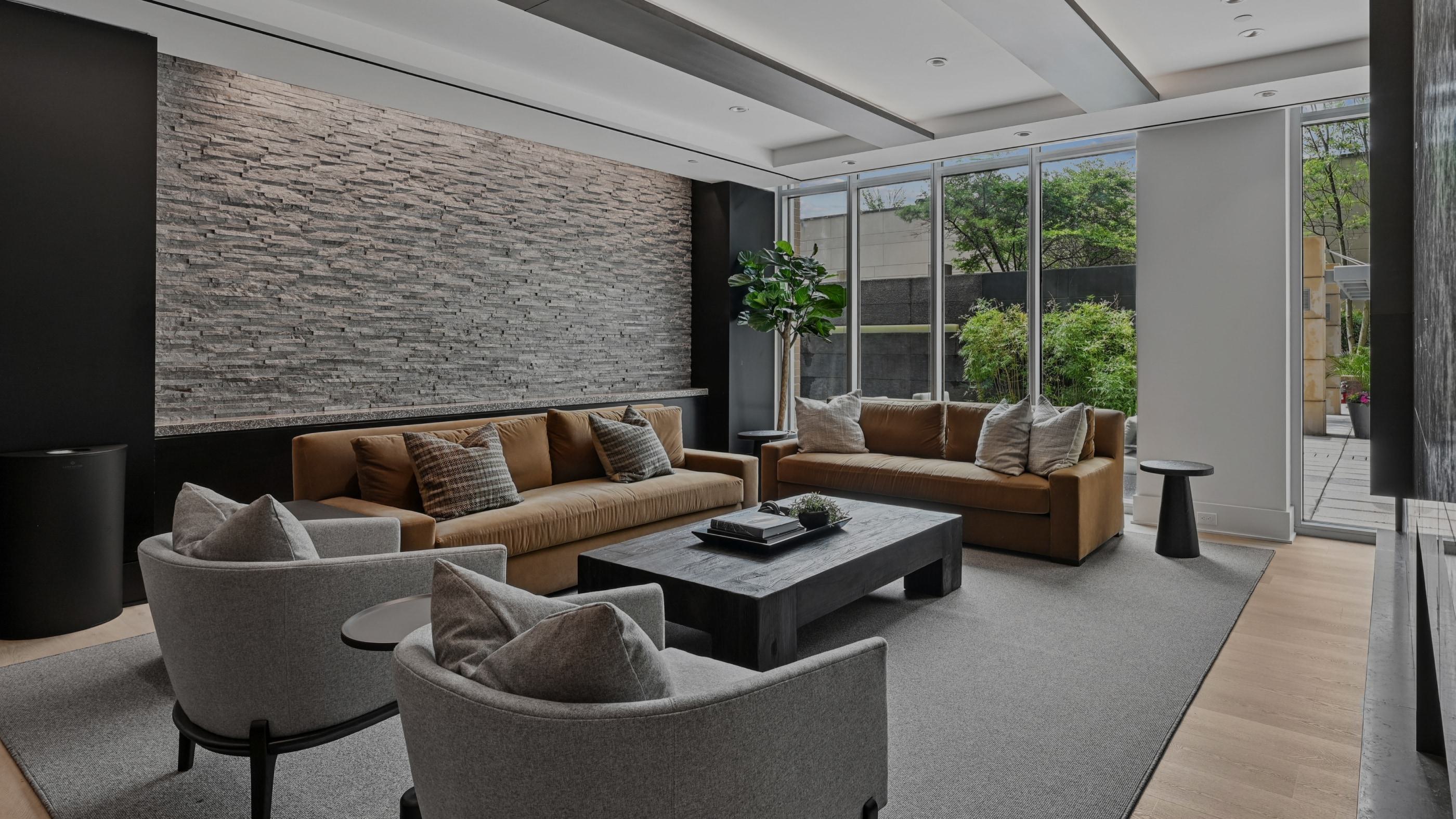 Modern resident lounge at Avant Reston featuring brown sofas, grey armchairs, a stone accent wall, and patio views.