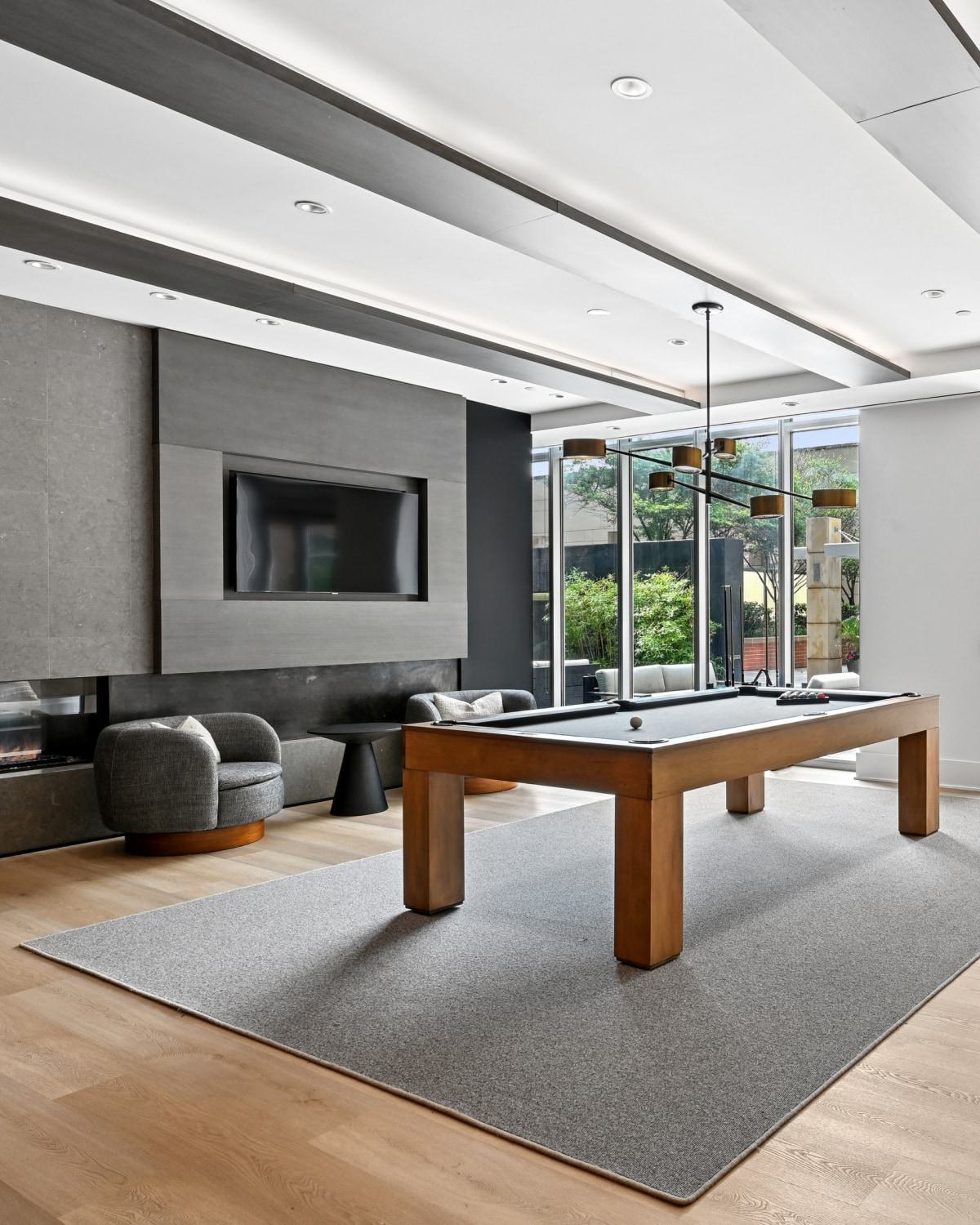Apartment game room at Avant Reston with a wooden pool table, a shuffleboard table, and glass doors opening to a patio.