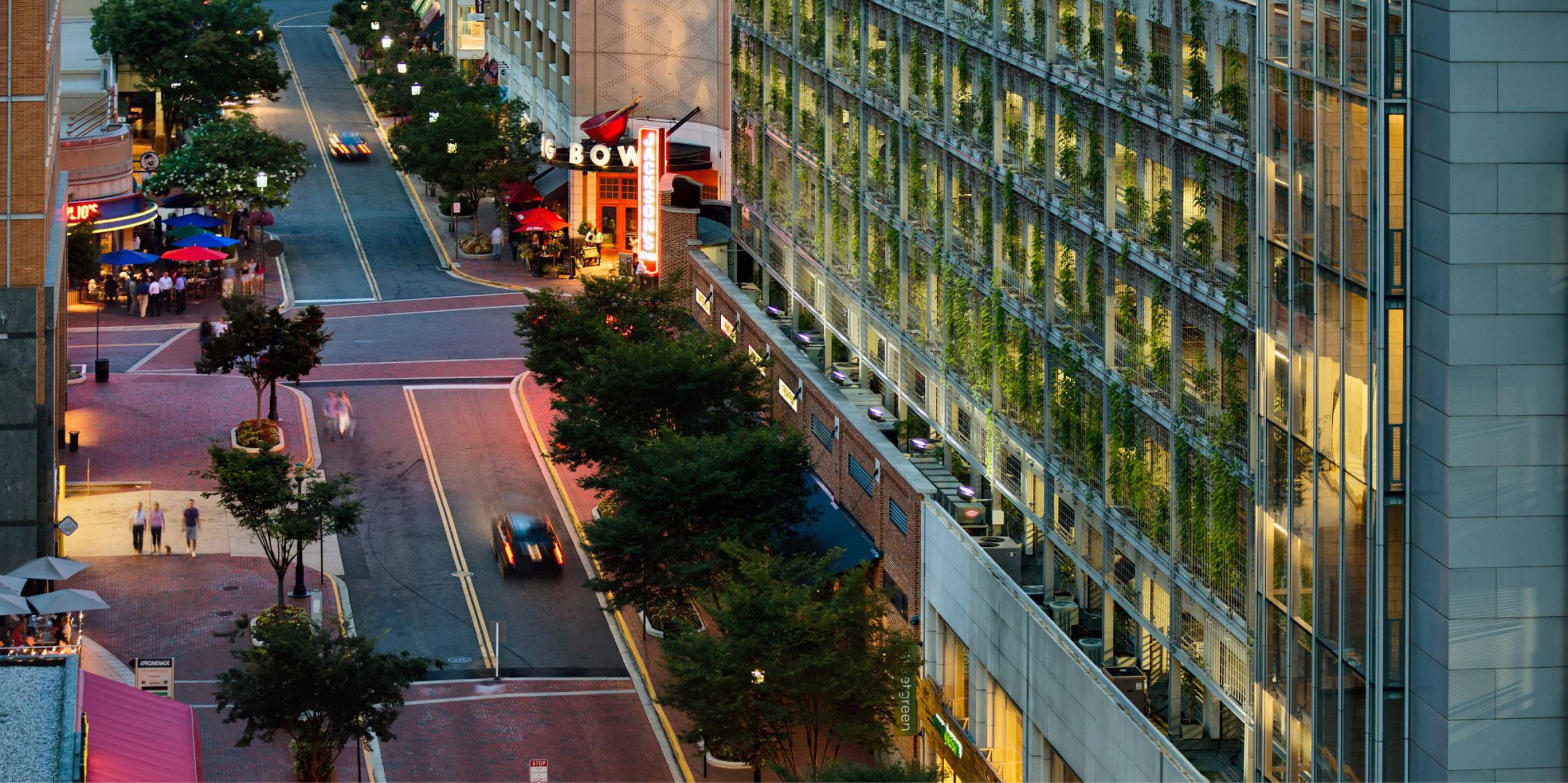 High-angle evening view of a Reston town center street with outdoor dining, storefronts, and a ivy-covered building façade.