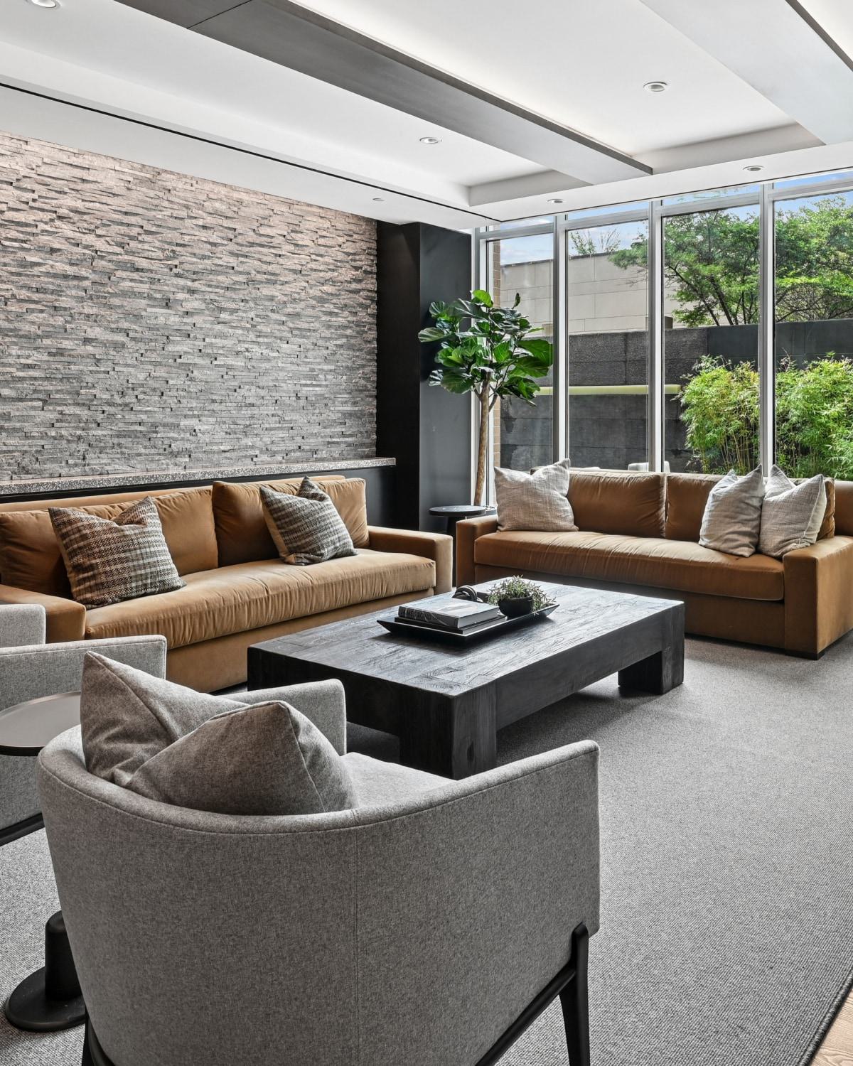 Modern resident lounge at Avant Reston featuring brown sofas, grey armchairs, a stone accent wall, and patio views.