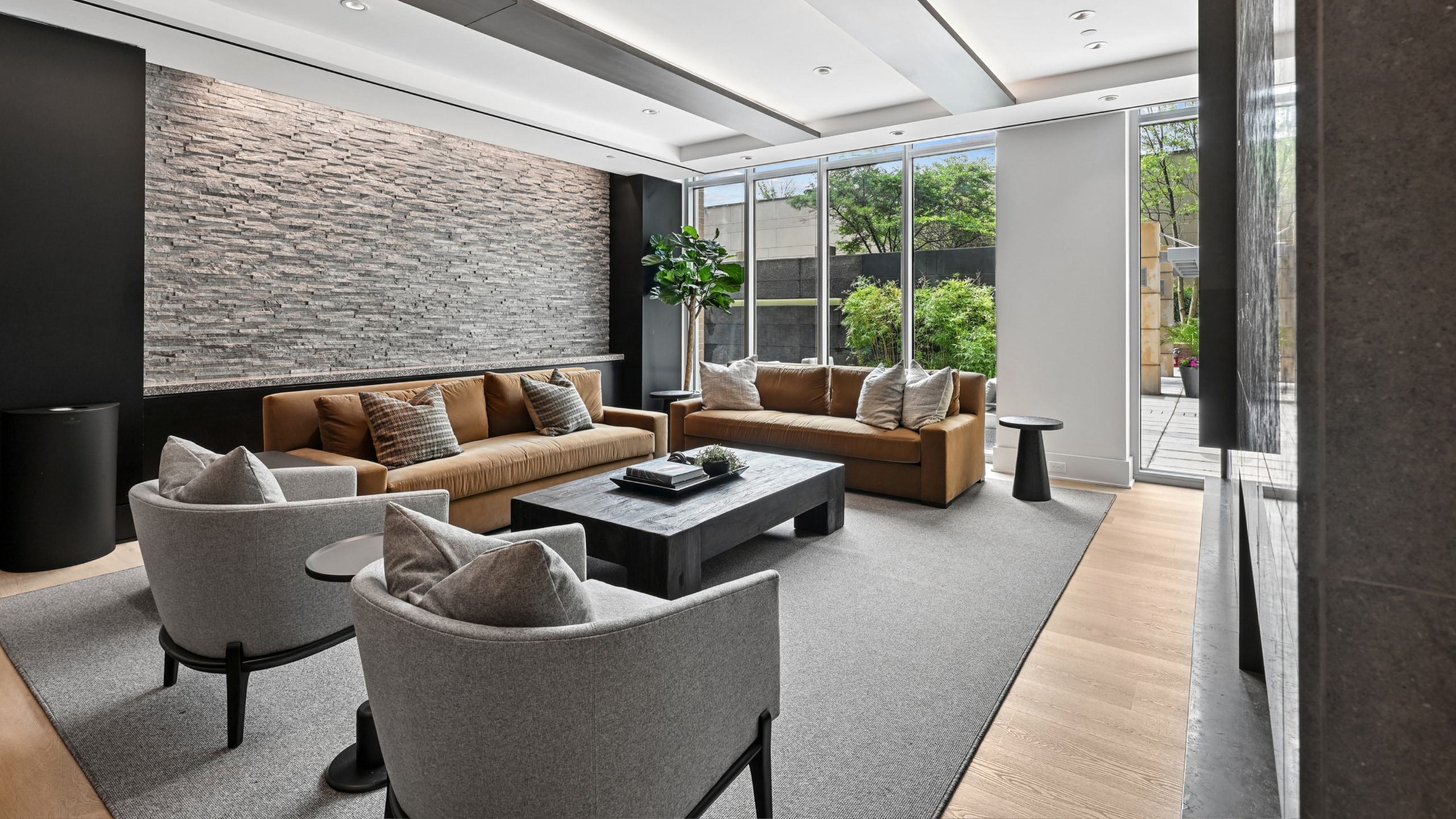 Modern resident lounge at Avant Reston featuring brown sofas, grey armchairs, a stone accent wall, and patio views.