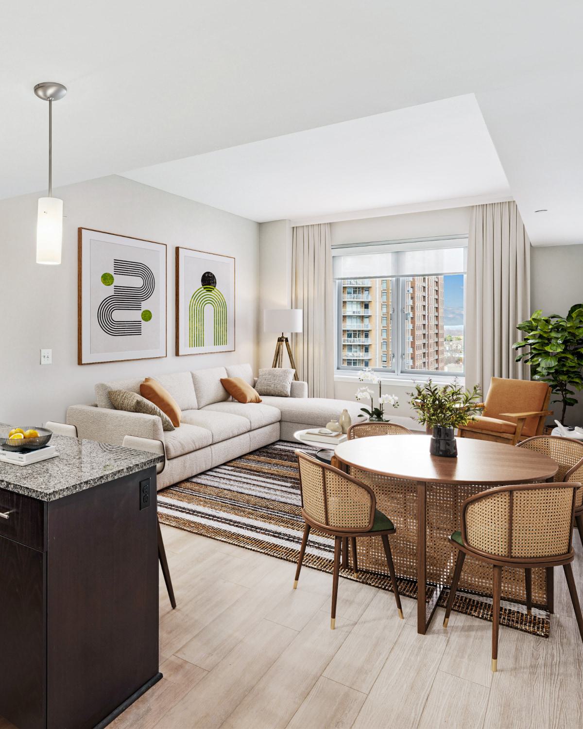 Modern apartment interior featuring a bright living room with a cream sectional sofa, abstract green and black wall art, a striped rug, and a round wooden dining table with woven cane chairs.