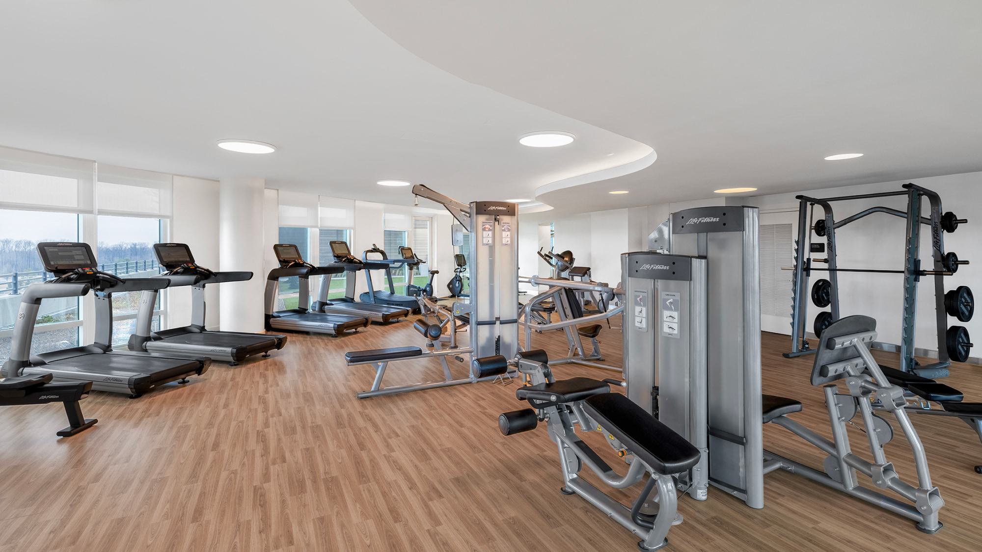Spacious gym at Adaire featuring cardio equipment, weight machines, benches, and large windows with natural light and skyline views.
