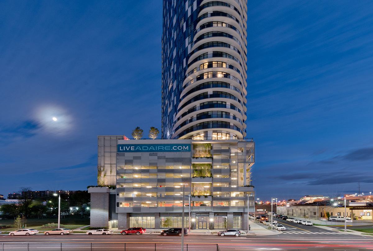 Exterior of Adaire high-rise in Tysons at dusk with illuminated covered parking garage and Spring Hill Metro nearby.