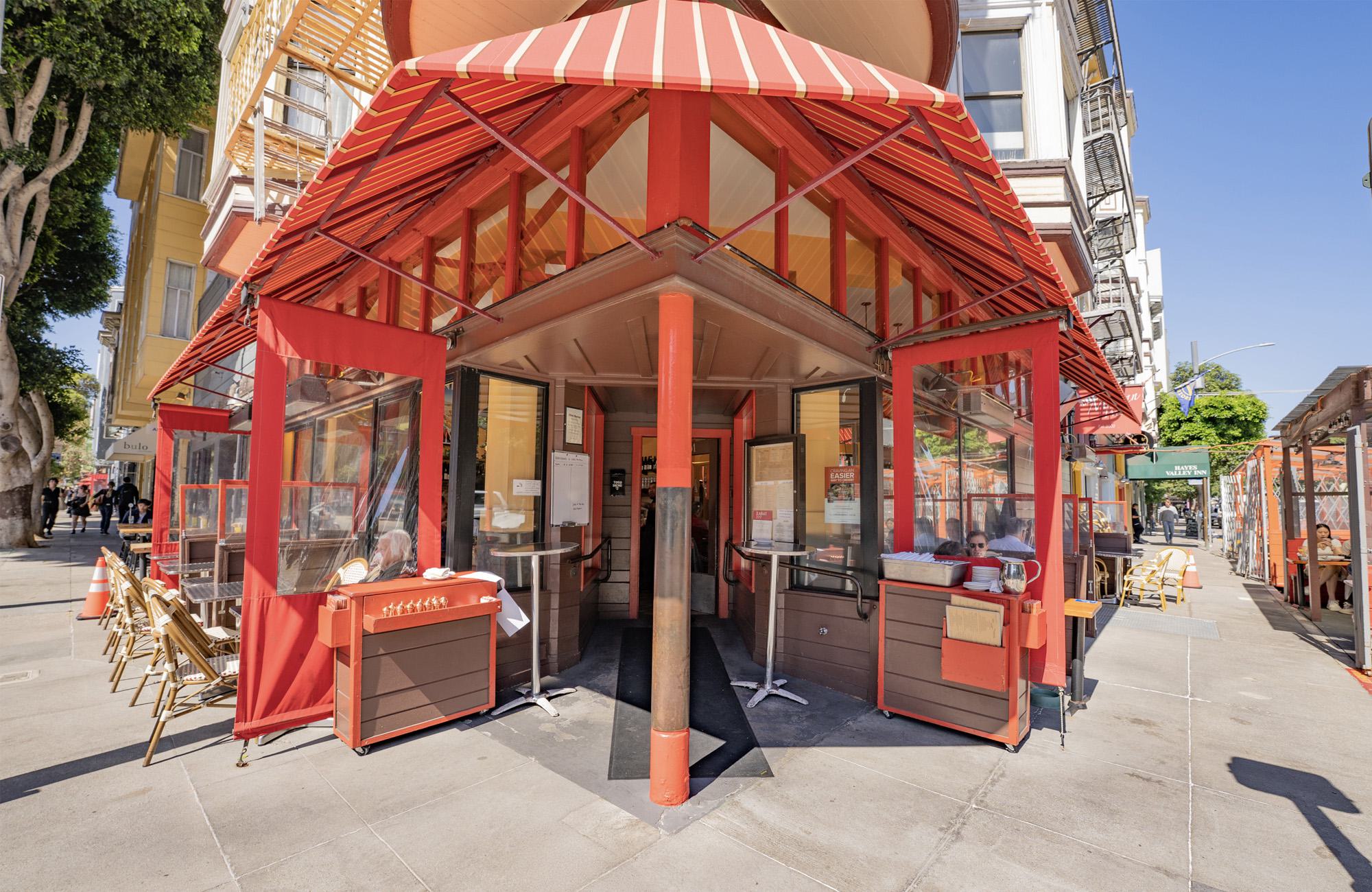 Chez Mama street corner restaurant in Hayes Valley with bold red striped awnings, outdoor sidewalk seating, and glass-enclosed patio dining on a sunny San Francisco day.