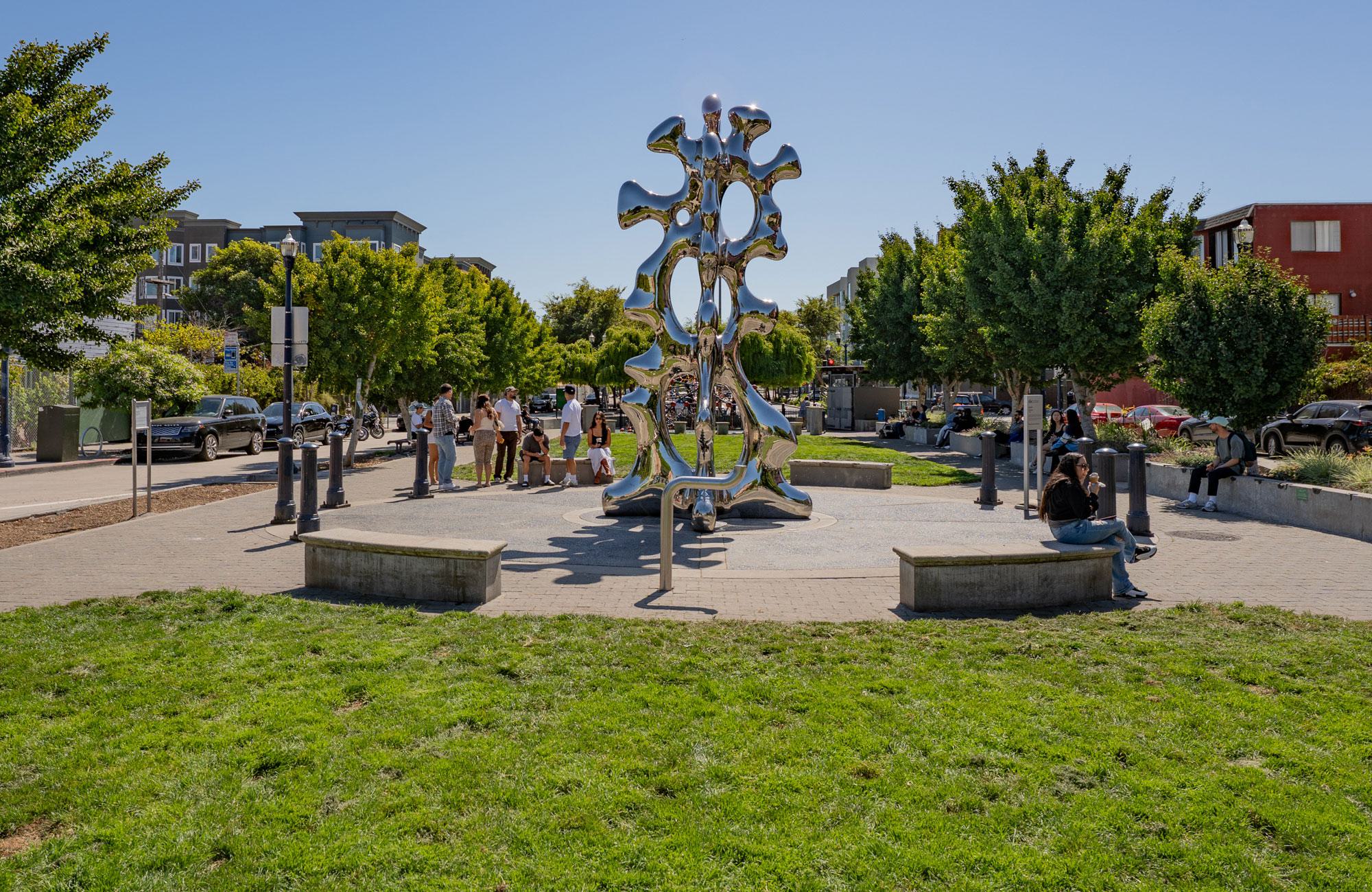 Public art sculpture at Patricia’s Green in Hayes Valley, with residents relaxing on benches and lawn under a clear San Francisco sky.
