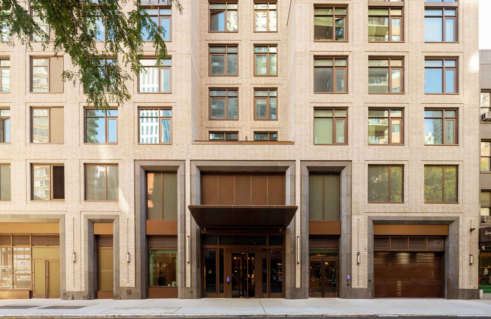 Street-level view of Maison 78 on East 78th Street featuring a brick façade, bronze canopy entrance, and integrated residential parking garage door.