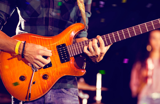 Musician playing guitar on stage with tambourine player in background