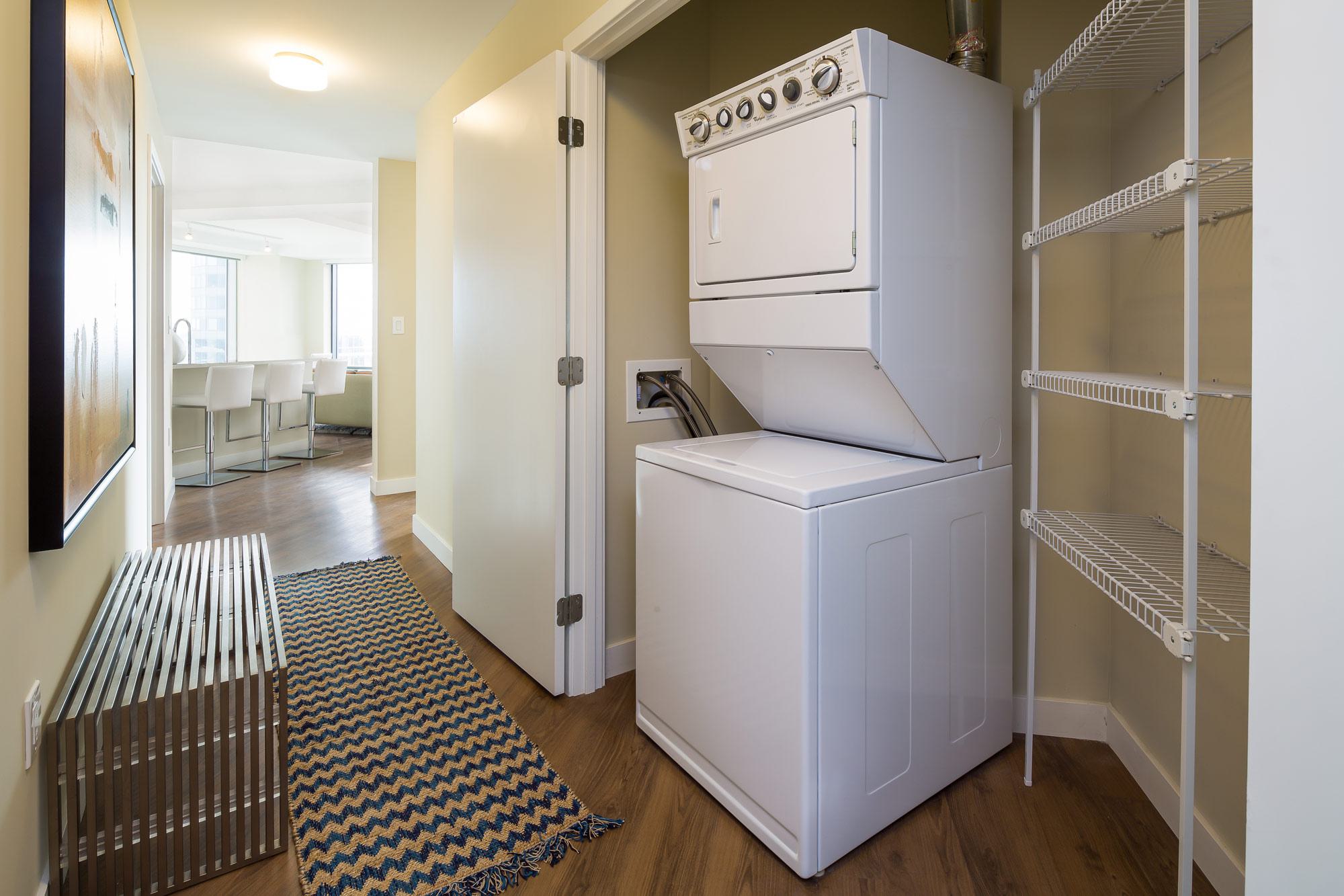 Stacked washer and dryer tucked into a discreet laundry closet at Luka on the Common, with built-in shelving for storage and easy access from the hallway.