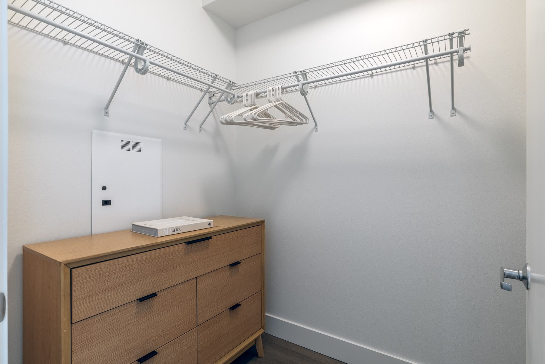 Walk-in closet at Urbana in Ballard with wire shelving, hanging rods, and a wood dresser for additional storage.