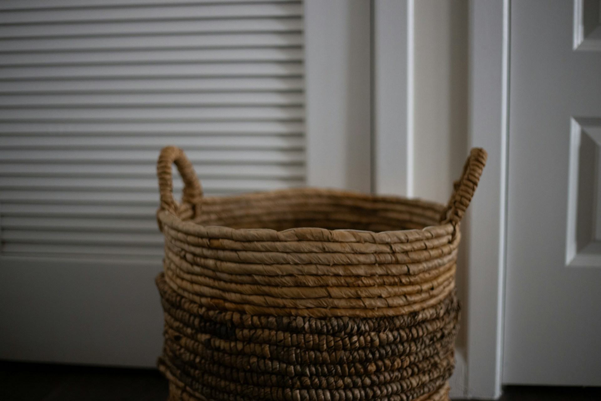 Woven laundry basket placed in front of a closet door concealing an in-home washer and dryer,