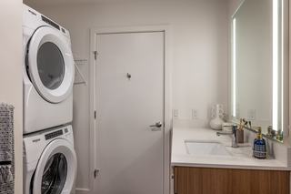 Stacked full-size Whirlpool front-loading washer and dryer installed beside the bathroom vanity in a modern Arlo apartment home.