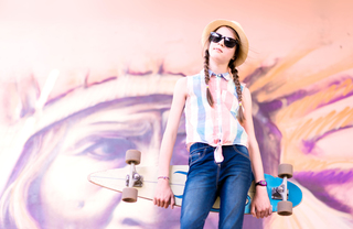 Girl with skateboard standing in front of an urban mural