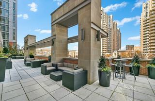 Outdoor lounge terrace at Avant Reston with cushioned seating under pergolas, bar-height table seating, planters, and views of nearby Reston Town Center towers.