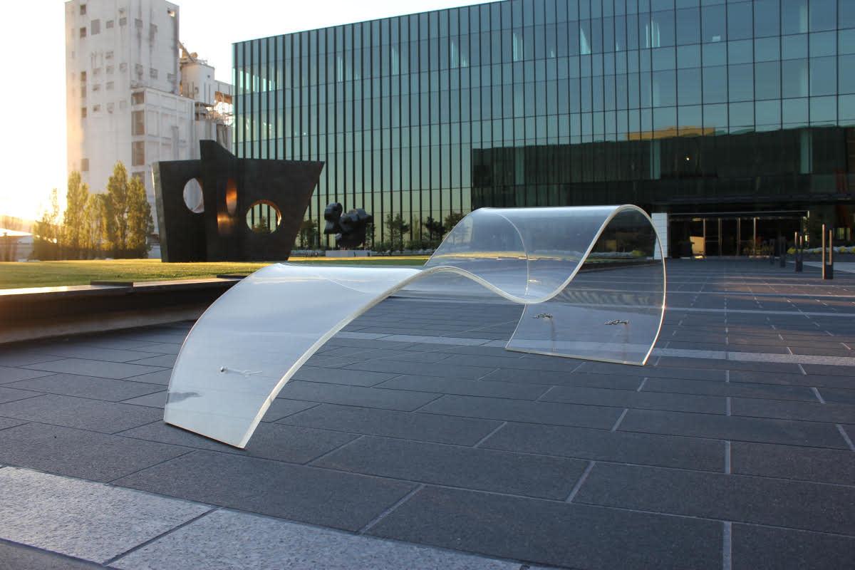 Transparent sculptural seating installation on the plaza outside the National Nordic Museum in Ballard, with modern glass architecture and public art in the background at sunset.