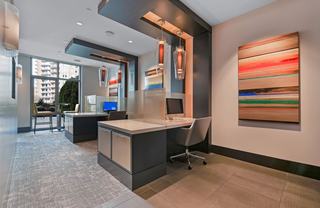 Modern coworking area at Avant featuring individual computer workstations with privacy dividers, pendant lighting, contemporary artwork, and large windows bringing in natural light.